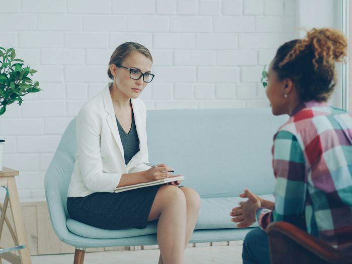A counselor takes notes while listening to a young woman during a private session