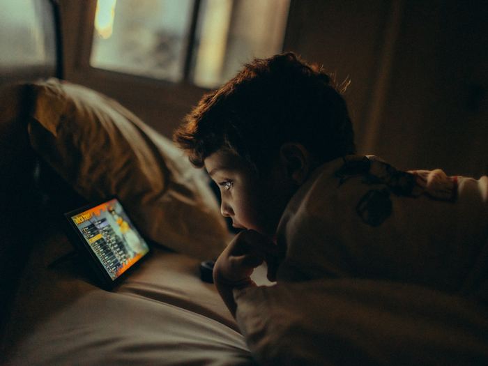 A young boy lies in bed at night, his face lit by the game on his tablet